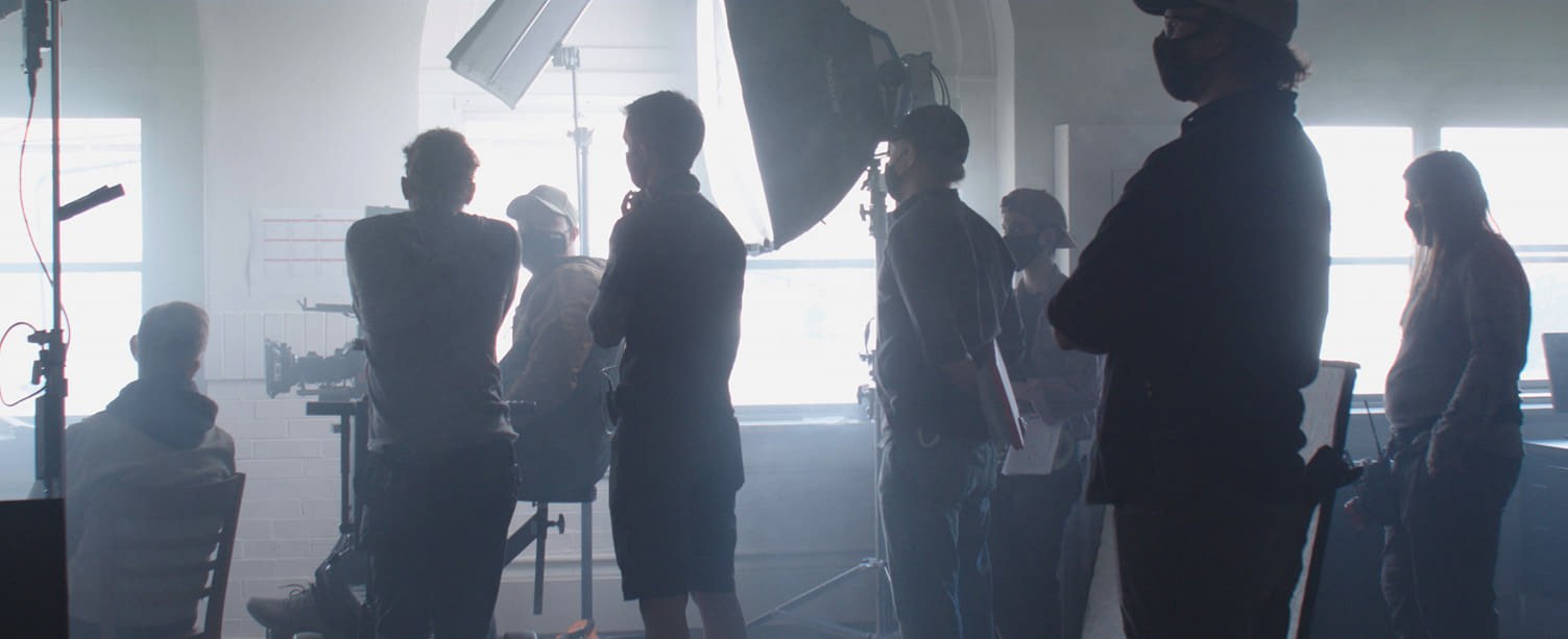 Silhouetted crew and film equipment in a bright hazy interior during As I Lie Awake production