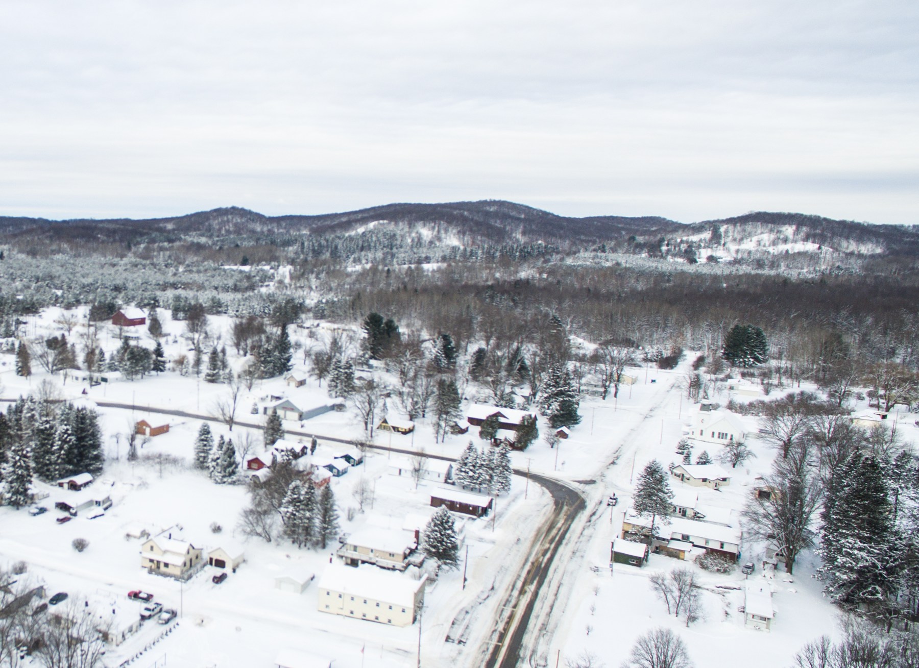 Aerial view of snow-covered houses, roads, and wooded hills in Harrietta, Michigan.