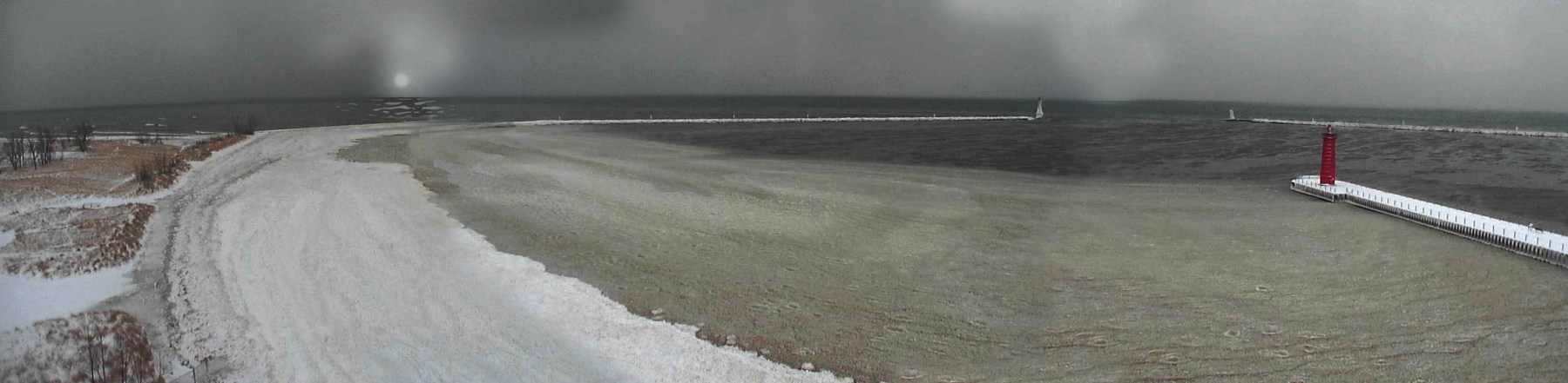 Wide gray winter panorama of the icy Muskegon channel and red pier light on Lake Michigan.