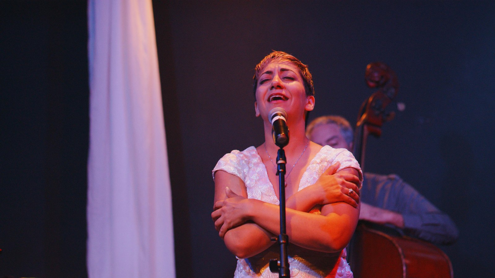 Shokoufeh singing into a microphone with a double bassist behind her